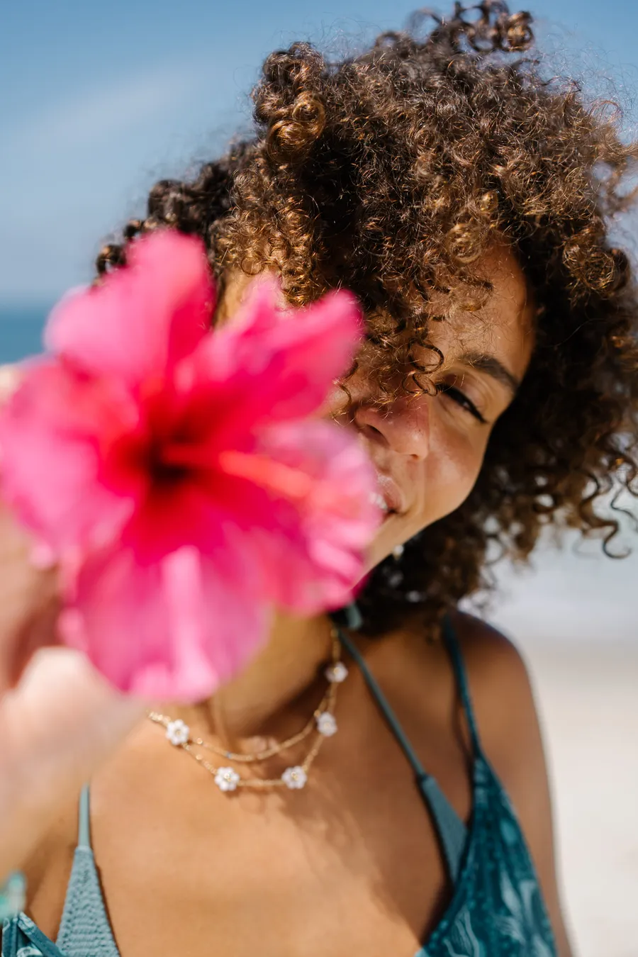 Model holding a pink hibiscus in front of her face on the beach