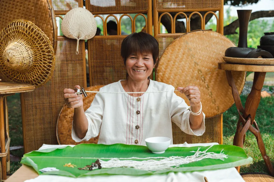 Artisan smiling while holding up a strand of hand-strung pearls