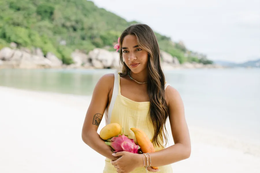 Model in a yellow dress holding tropical fruit on a beach