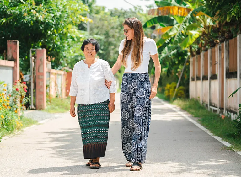 Two women in printed sarongs walking arm in arm down a village lane